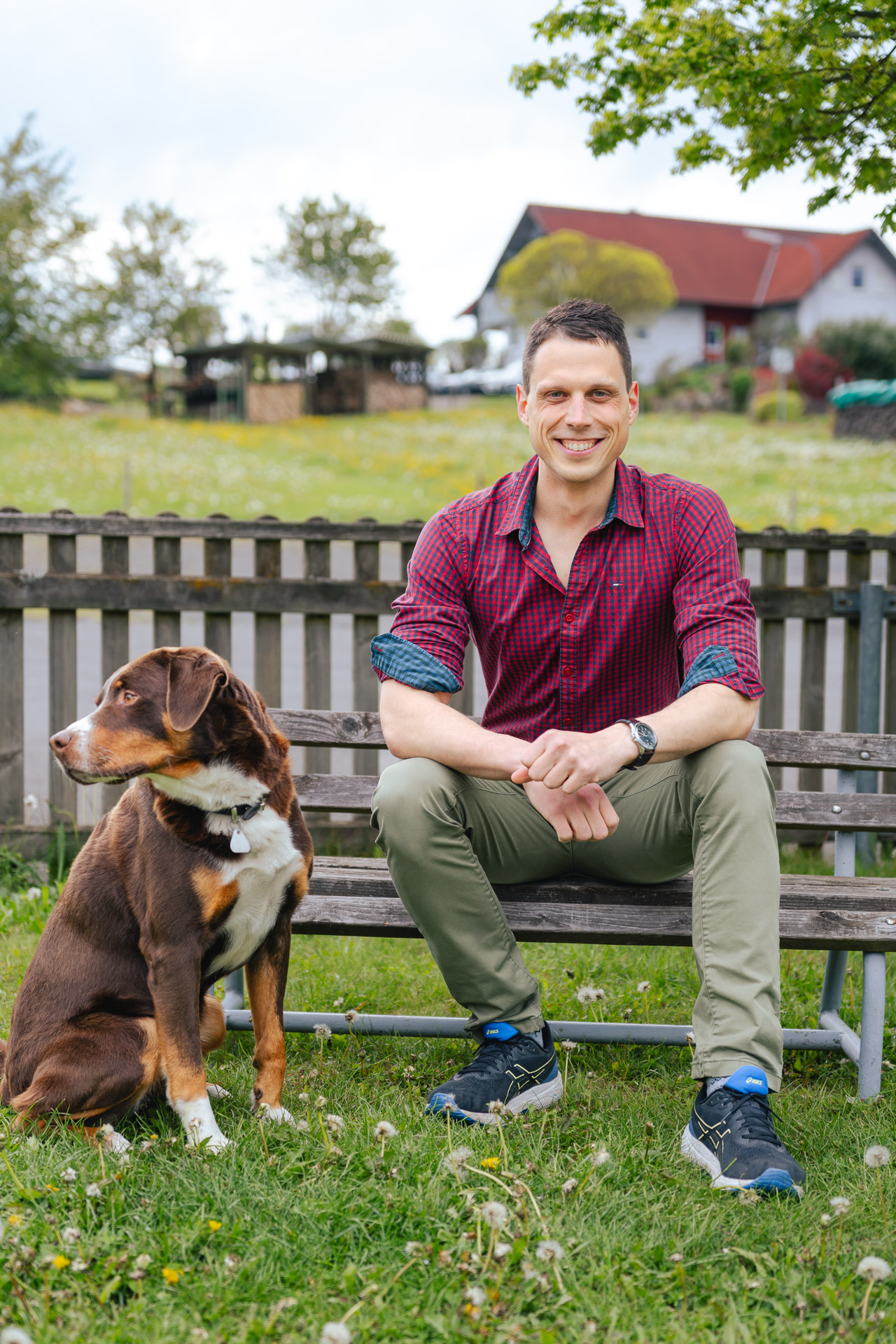 Mann sitzt mit seinem Hund auf einer Bank vor einem Bauernhaus